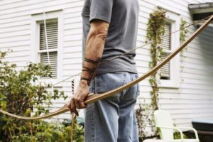 Mann haelt Langbogen und Pfeil in der Hand