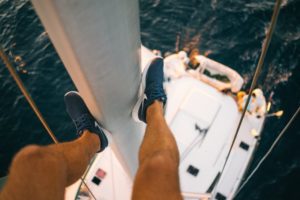 Junger Mann mit Segelschuhen hängt an einem Segelmast
