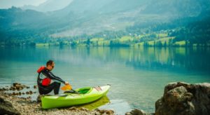 Kanufahrer sitzt in Paddelhosen am See.