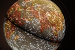 Ein Globus ist mit weißen Linien der Sternzeichen an unserem Himmelszelt überzogen. Die Landmassen sind in rot-gelb Tönen gehalten, der Hintergrund ist schwarz.