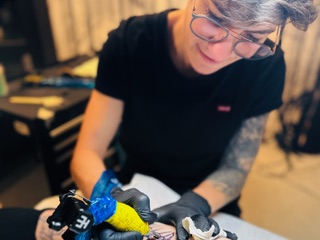 Tattoo-Künstlerin arbeitet an einem Tattoo, während sie konzentriert mit einer Maschine tätowiert.