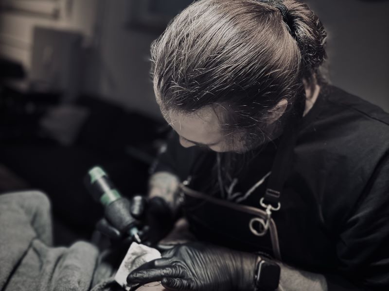 Tattoo-Künstler arbeitet konzentriert an einem Tattoo, während er die Maschine führt.