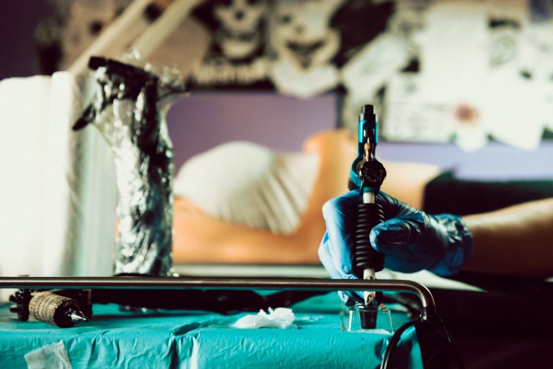Tattoo-Künstler arbeitet an einem Tattoo mit einer Maschine, während der Kunde auf der Liege liegt.