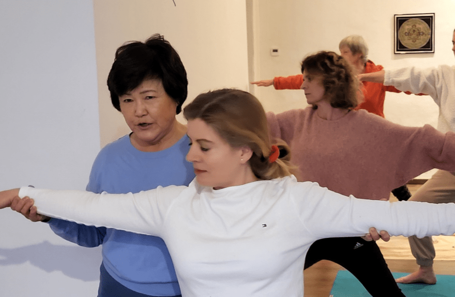 Eine Yogalehrerin unterstützt eine Teilnehmerin bei der korrekten Ausführung einer Asana in einer Yoga-Klasse.